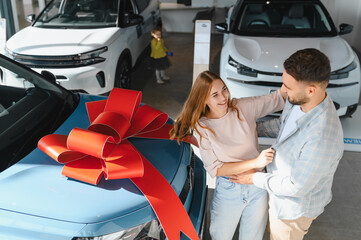 Couple celebrating buying new car with red bow gift