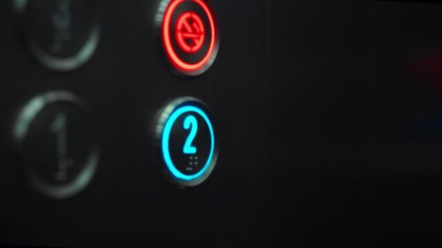 A man's finger presses the button marked '2' in a sleek elevator. The action suggests he is moving to the second floor of a contemporary office or residential building