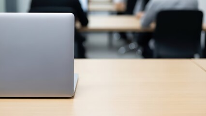 Open laptop on wooden desk in modern office with blurred colleagues
