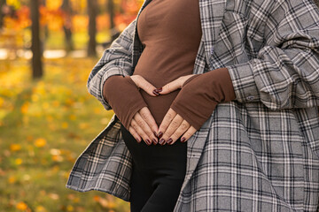 Pregnant woman making heart shape on belly in autumn