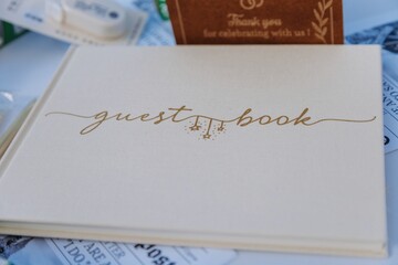 Elegant beige wedding guest book with gold lettering on white table with stationery.