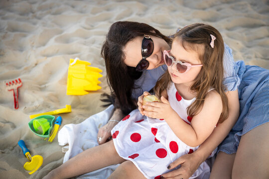 Mother and daughter playing with sand toys on the beach, looking lovingly at each other.