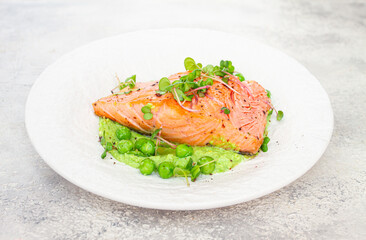 Grilled salmon filet served on a bed of green pea puree with fresh microgreens and peas, presented on a white plate