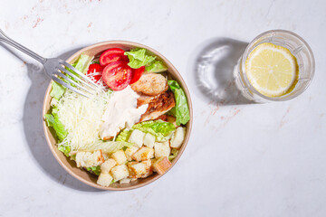 Caesar salad, in a disposable paper container, with a fork on the table, hard light,