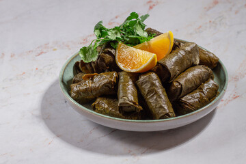 grape leaves stuffed with minced meat with rice, herbs and spices on a plate with slices of fresh lemon,