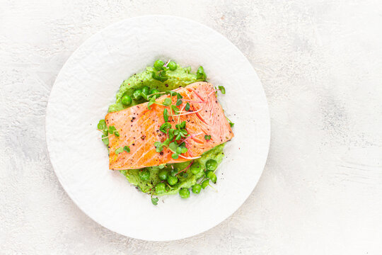 Grilled salmon filet served on a bed of green pea puree with fresh microgreens and peas, presented on a white plate
