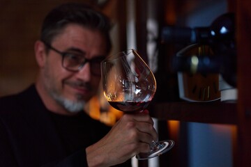 Middle aged man tasting, drinking wine in cellar. Wine expert rating a glass of red wine. Professional sommelier satisfied.
