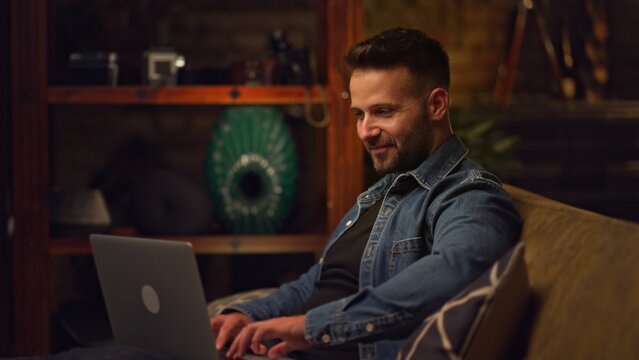 Businessman working from home on laptop computer. Happy young man sitting on couch in home office with laptop.