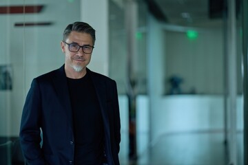 Business portrait - businessman standing on office corridor. Happy middle aged, mid adult, mature age man smiling. Entrepreneur in modern workplace. Copy space.