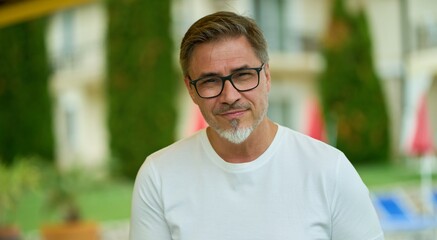 Portrait of happy middle aged man at home in front of house, confident, smiling. Outdoor in garden of villa, residence.