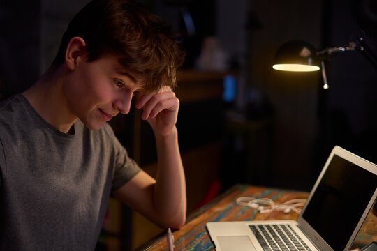 Teenage student learning at home with books and laptop computer. Online school and education, sitting at desk late night