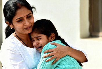 Indian mother comforting her crying daughter with a hug. A loving parent offers emotional support to her sad child. Motherhood and family care concept