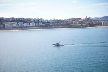 Fototapeta premium Motorboat crossing bay of San Sebastian with city skyline and beach in background, Spain
