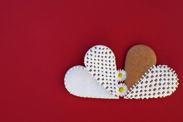 Gingerbread hearts decorated with white icing, with daisy flowers, red background, copy space for...