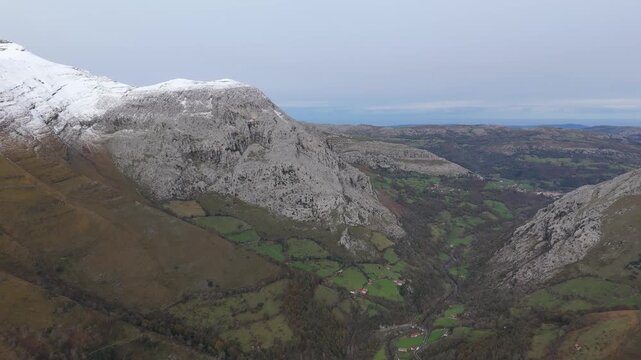 Green forests nestle in Val del As&oacute;ns deep valley, Cantabria - Here is a revised description that meets the stock photography style guidelines: Mountain landscape featuring a village in background.