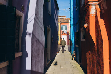 Man walking colorful alley in Burano Venice Italy