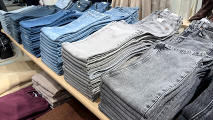 Neatly folded stacks of blue gray denim jeans displayed on wooden shelf in modern clothing store. clean layout, detailed fabric texture, and organized presentation create a stylish retail atmosphere.