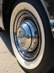 Close-up of a vintage car wheel showcasing chrome details and whitewall tires in a sunny setting