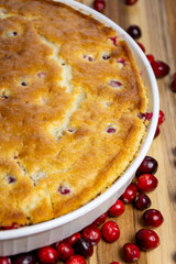 Rustic close-up of a freshly baked cranberry cake showing the golden, cracked crust and edge of the dish on a dark wood board. Cozy homemade food.