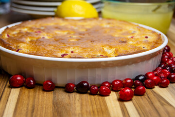 Freshly baked cranberry cake in a rustic dish, surrounded by scattered fresh cranberries and lemon. Homemade holiday dessert on dark wood.