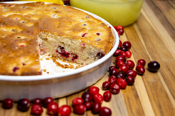 Homemade cranberry cake remaining in the baking dish after a slice was served, showing the moist crumb and golden crust edges. Cozy dessert.
