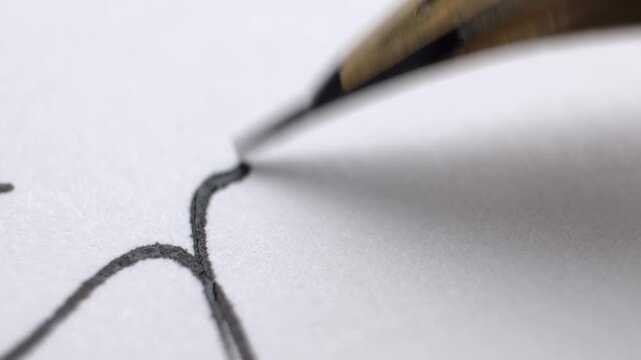 Close up of an antique calligraphy pen nib writing a thick black line. Slow motion of a classic vintage fountain pen drawing a curvy lines with ink absorbed by the parchment paper.