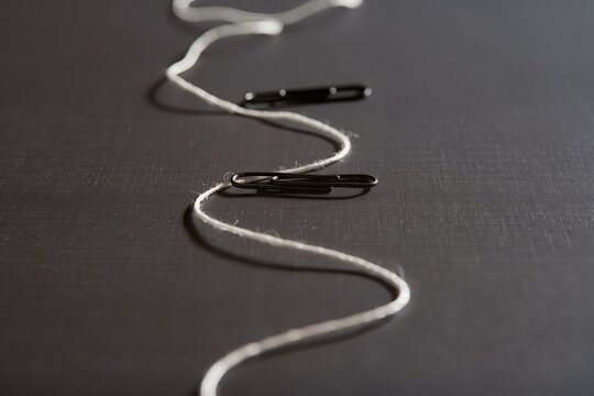Creative arrangement of thread and clips on a dark surface during a crafting session in the afternoon light