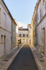 A narrow alleyway with a brick walkway and a few buildings in Saintes France. The buildings are white and have shutters on the windows