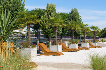A promenade with wooden red loungers in the city of Saintes, France The area is covered with sand; a huge Catholic church is visible in the background. The sky is blue and clear