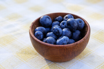 A rustic wooden bowl, filled with fresh blueberries, sits on a delicate tablecloth. A great fit for promotions related to health and dieting. Copy space