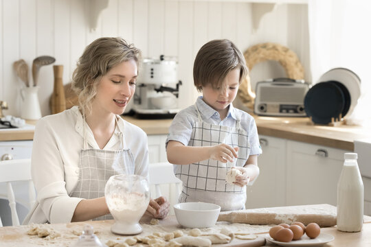 Focused little son learn to make pies imitating caring mom