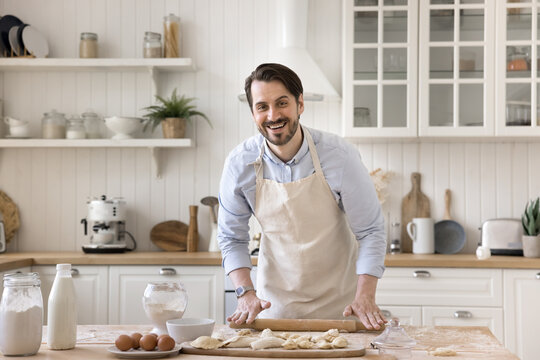 Portrait joyful man in apron smiling at camera flattening dough