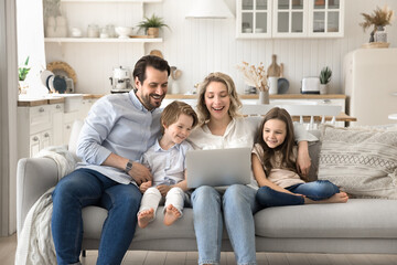 Joyful laughing couple with small children watching videos on notebook