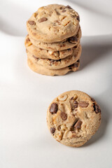 A stack of cookies with nuts on top of a white textured background. A single cookie is in the foreground on table