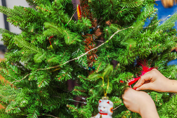 Close up view of child decorating Christmas tree with festive ornaments inside cozy home during holiday season. Sweden.