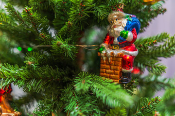 Close up view of Santa ornament sitting on chimney among green branches of Christmas tree. Sweden.