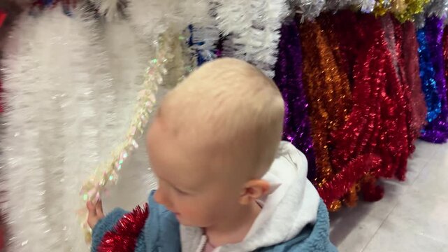 Little smiling child runs between multicoloured Christmas tinsel. Christmas holidays content. 4K