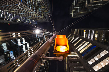 Fototapeta premium A glowing urban traffic light hangs above the street like a small sun, framed by looming skyscrapers that tilt inward, creating a dramatic tunnel of glass and steel against the night sky.