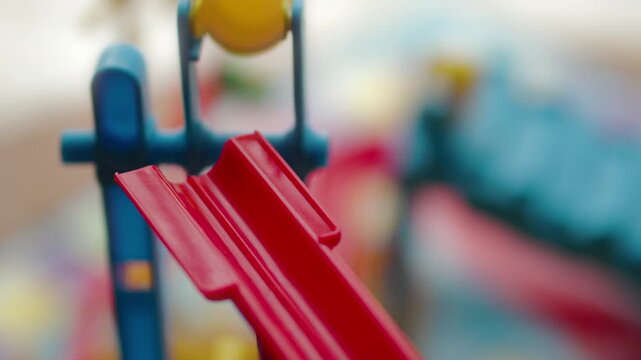 Close-up of a silver, metallic marble ball falling out of a plastic bucket, down a red slide (board game)