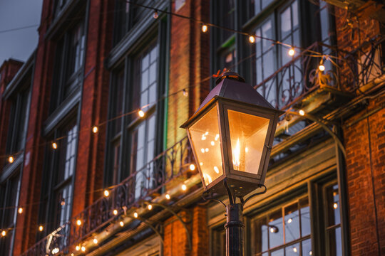 Warm street lantern glowing at dusk in Toronto's historic Distillery District, with festive string lights illuminating the old brick architecture.