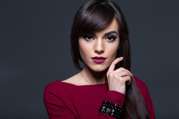 High-Fashion Studio Portrait of an Elegant Brunette Woman in a Burgundy Off-the-Shoulder Dress, Featuring Bold Smokey Eyes and Dark Lipstick