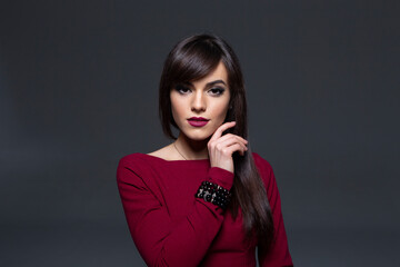 Close-Up Studio Portrait of a Serious Brunette Woman with Smokey Eye Makeup and Dark Lipstick, Posing with Hand Touching Jawline.