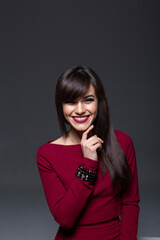 Studio Headshot of an Elegant Brunette Model with Dark Smokey Eyes and Serious Expression, Posing with Finger Near Chin and Wearing a Maroon Top on a Dark Grey Background