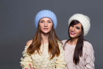 Waist-Up Shot of Two Female Models Displaying Warm Autumn or Winter Knitwear, Featuring a Blue Mohair Hat and Off-Shoulder Yellow Sweater Next to a White Ribbed Beanie and Patterned Beige Pullover