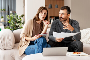 Couple discussing finances and planning home budget sitting on comfortable sofa at home