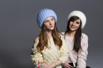 Waist-Up Shot of Two Female Models Displaying Warm Autumn or Winter Knitwear, Featuring a Blue Mohair Hat and Off-Shoulder Yellow Sweater Next to a White Ribbed Beanie and Patterned Beige Pullover