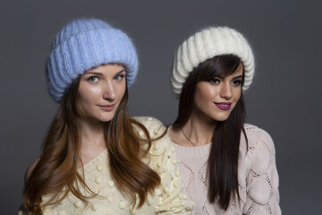 Joyful Holiday or Winter Concept Photo of Two Girls Having Fun, Wearing a Blue Fluffy Beanie and a White Ribbed Hat, Isolated on a Neutral Background