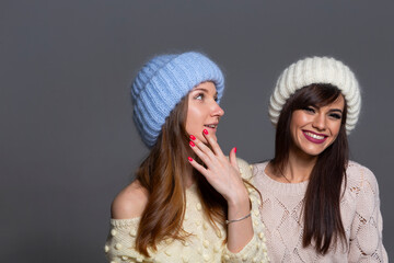 Joyful Holiday or Winter Concept Photo of Two Girls Having Fun, Wearing a Blue Fluffy Beanie and a White Ribbed Hat, Isolated on a Neutral Background