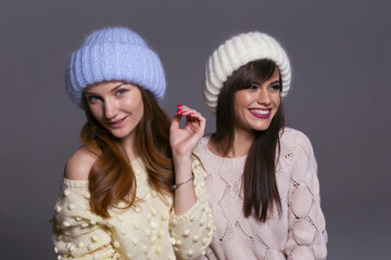 Joyful Holiday or Winter Concept Photo of Two Girls Having Fun, Wearing a Blue Fluffy Beanie and a White Ribbed Hat, Isolated on a Neutral Background