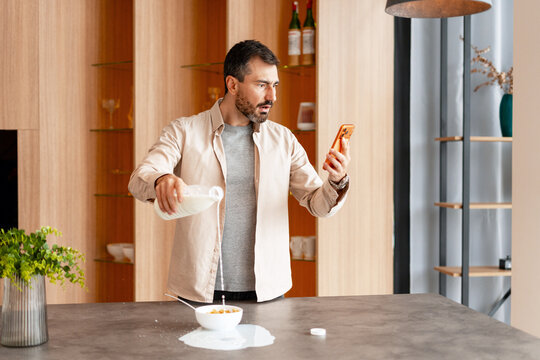 Man spilling milk while distracted by mobile phone